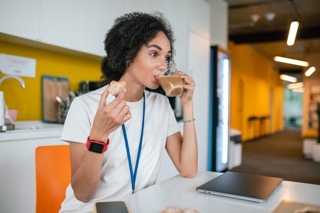 食堂の中で。オフィスの食堂でコーヒーを作るオフィスの若い黒髪の女性