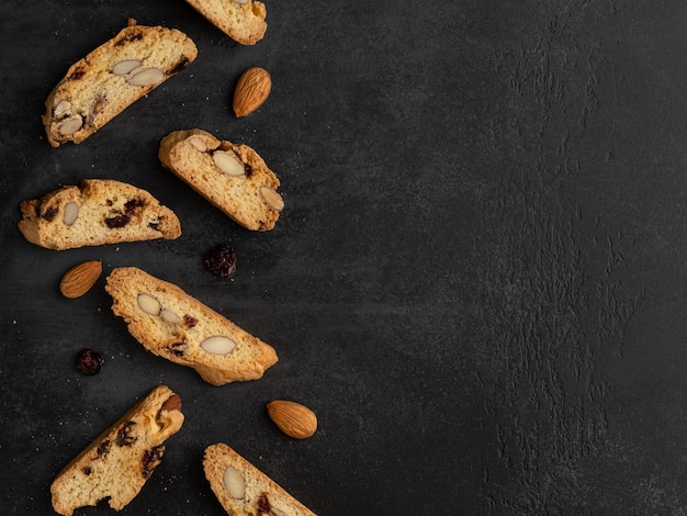 Cantucci (italian double baked cookies, biscotti) with orange zest, almond nuts and dried cranberry.. Flat layout, top view, place for text. Dark background.