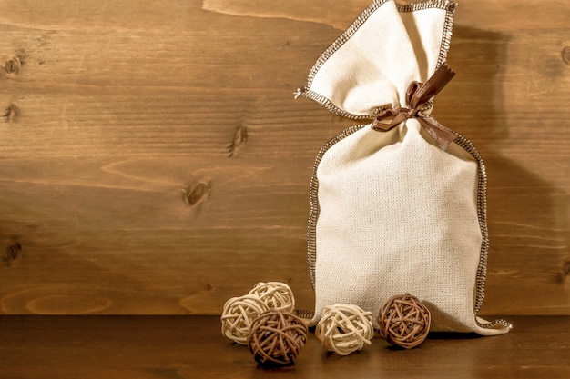 Canvas bag with gifts next to small wicker decorative balls, on brown wooden background. Concept: gift for the new year, christmas, postcard. Copy space.