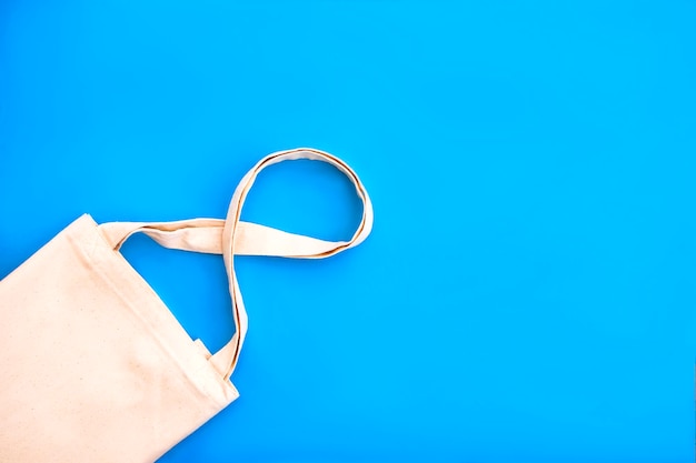 Canvas cotton white bag on the bright blue background. Eco Friendly reusable bag for groceries and shopping. Eco and zero waste concept. Close up.