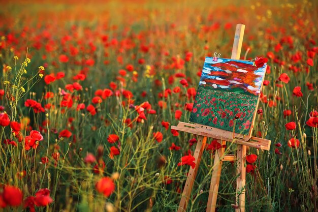 Canvas met een geschilderde afbeelding in een veld met rode klaprozen bij zonsondergang