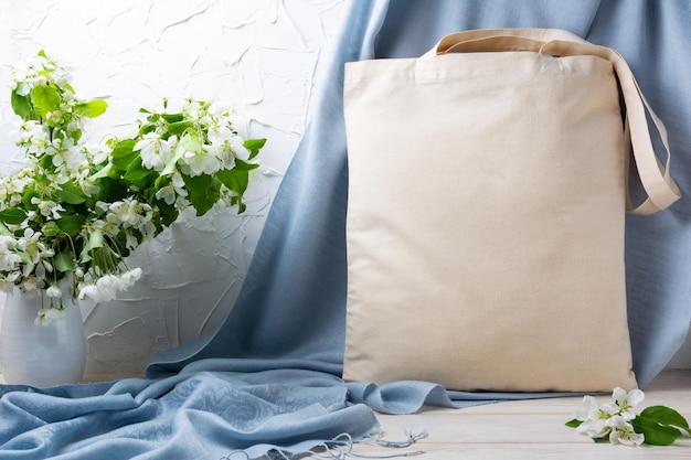 Canvas tote bag mockup with apple blossom branches and blue scarf Rustic linen shopper bag mock up for branding presentation