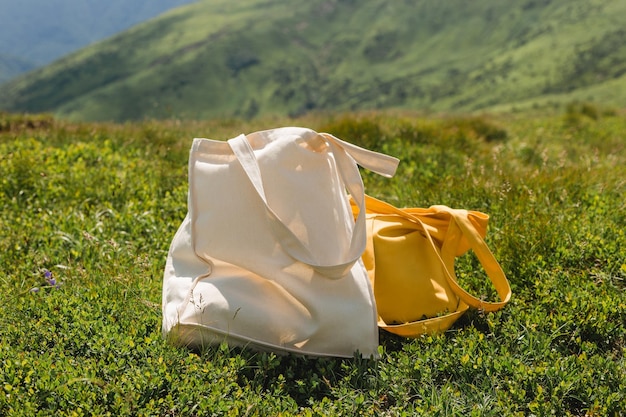 Photo canvas tote bags on green grass on the edge of the hill in the park eco nature friendly style environmental conservation recycling concept mockup