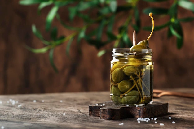 Capers Marinated or pickled canned capers fruit in glass jar on wooden table background Space for text