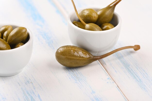 Capers in a white little bowl on the white background