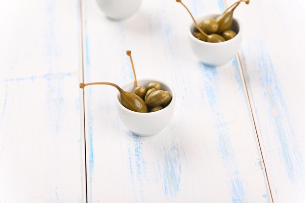 Capers in a white little bowl on the white background