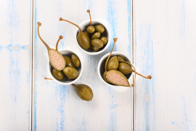 Capers in a white little bowl on the white background