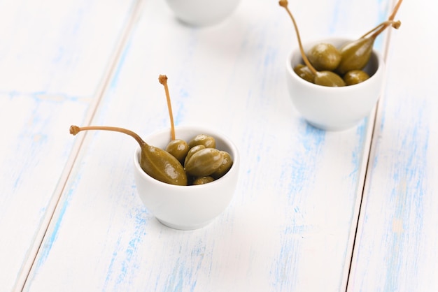 Capers in a white little bowl on the white background