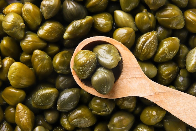 Capers in a wooden spoon background Top view