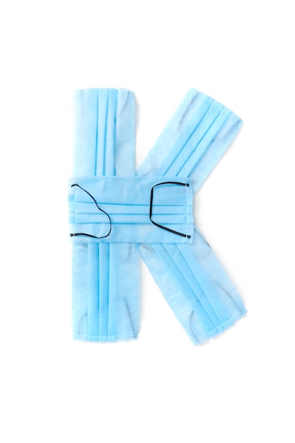 Capital letter K handmade from medical antibacterial protective blue face masks on a white wall, copy space. Creative alphabet for making up new words.