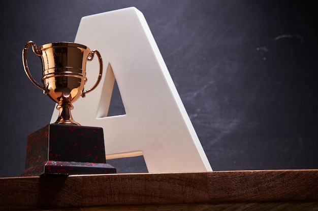 Capital letter A and wining trophy against blackboard