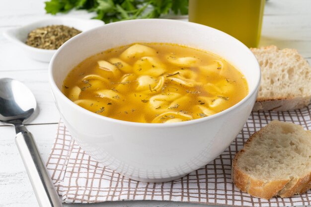 Cappelletti of tortellini brodo-soep in een kom met sneetjes brood en kruiden op houten tafel