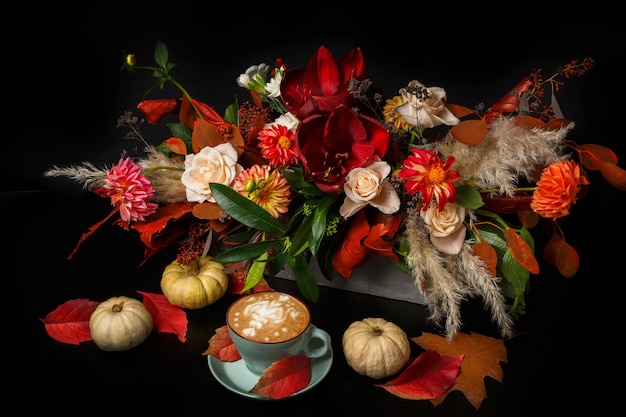 Фото Капучино и красивые цветы натюрморт. состав цветочного магазина. чашка кофе с пеной, яблоком, букетом свежих и сушеных цветов на черном деревянном столе. флористическое искусство и концепция цветочного дизайна