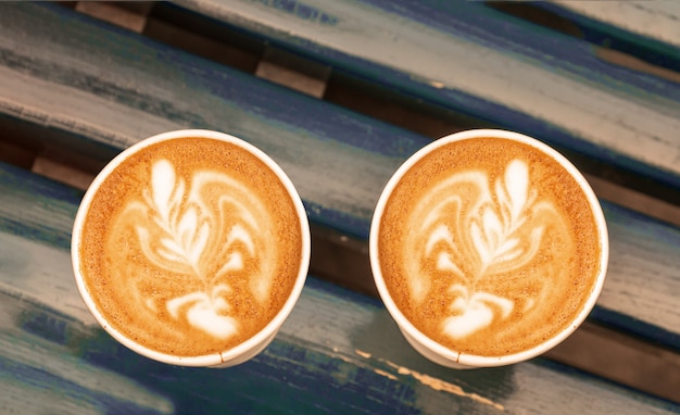 Cappuccino coffee latte art in paper cups on wooden bench, outdoor.