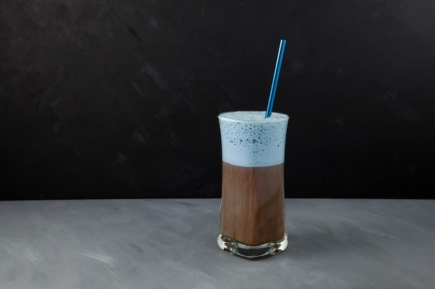 Cappuccino coffee or latte with blue milk foam in tall glass.