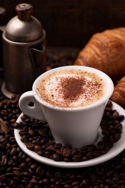 Cappuccino and croissant with coffee beans close up