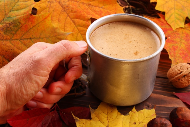 Напиток капучино в чашке в руке осенью