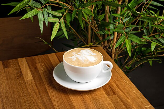 Cappuccino in een witte kop op een houten tafel in een restaurant groene plant op de achtergrond