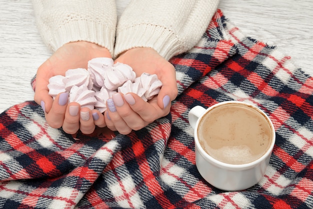 Photo cappuccino and meringue in female hands, checkered plaid. fashionable concept