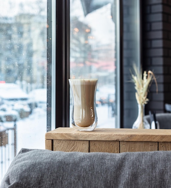 Foto cappuccino met melkschuim in glazen beker op houten tafel in café of koffiehuis.