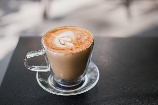 Cappuccino met room in een transparante kop op zwart bureau