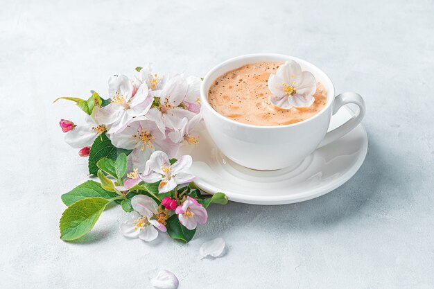 Cappuccino in a white cup and flowers on a gray wall. Side view. A greeting card.