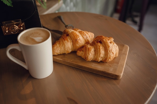 Cappuccino con bella arte del latte e croissant su fondo di legno sul tavolo. colazione perfetta al mattino. stile rustico.