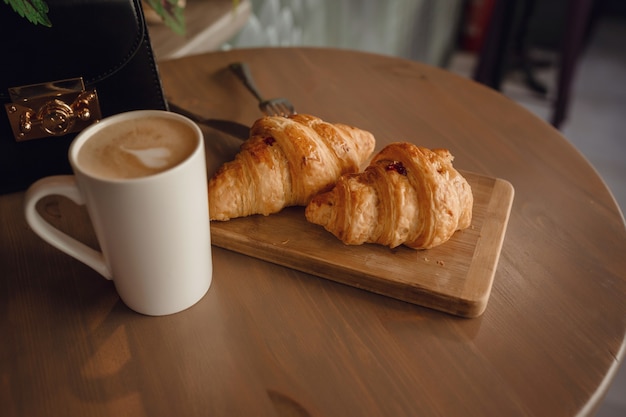 テーブルの上の木製の背景に美しいラテアートとクロワッサンのカプチーノ。朝の完璧な朝食。素朴なスタイル。