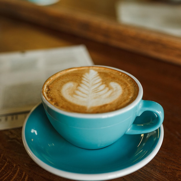 cappuccino with coffee art and soft froth in cup served on wooden table in coffee shop