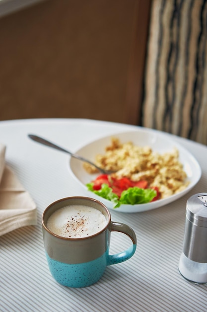 Cappuccinokoffie in kop en bord met roerei en tomatenontbijt op tafel