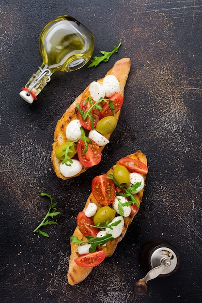 오래된 어두운 표면에 체리 토마토, 모짜렐라, 올리브 및 바질을 곁들인 Caprese bruschetta 토스트. 평면도.