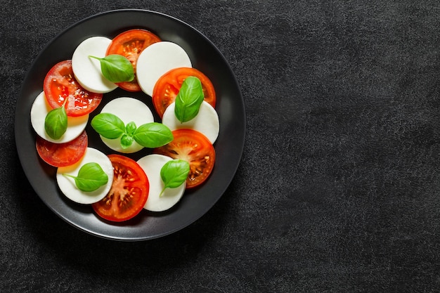 Caprese Italian antipasto tomato mozzarella and basil appetizer on dark background top view space to copy textxA