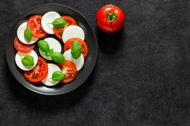 Caprese Italian antipasto and whole tomato on dark background top view space to copy textxD