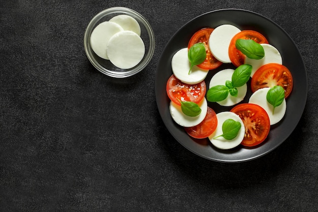 Caprese Italian appetizer of mozzarella basil and tomatoes on gray plate on dark background top view space to copy text