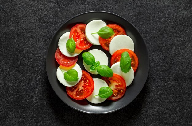 Caprese Italian appetizer on plate on dark background top view space to copy text