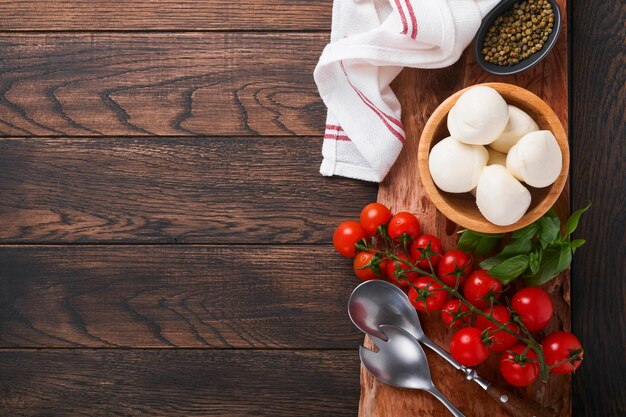 Caprese salad ingredients for cooking Cutting wooden board with traditional caprese preparation ingridients mozzarella tomatoes basil olive oil cheese spices on wooden rustic background