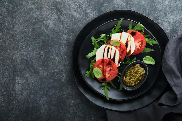 Caprese salad italian caprese salad with sliced tomatoes\
mozzarella cheese arugula basil olive oil in black plate over old\
brick tiles black background delicious italian food top view