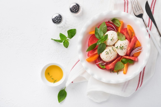 Caprese salad Italian caprese salad with sliced tomatoes mozzarella cheese basil olive oil in white plate over white background Delicious Italian food Top view Rustic style