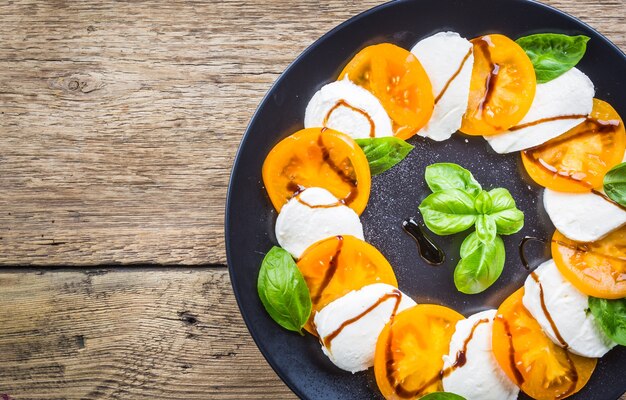 Foto caprese salade gemaakt van mozzarellakaas, gele tomaten en basilicumblaadjes op een houten ondergrond. bovenaanzicht.