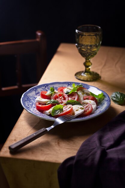 Caprese salade. Italiaanse beroemde salade met verse tomaten, mozzarellakaas en basilicum. Donkere en humeurige stijlfoto