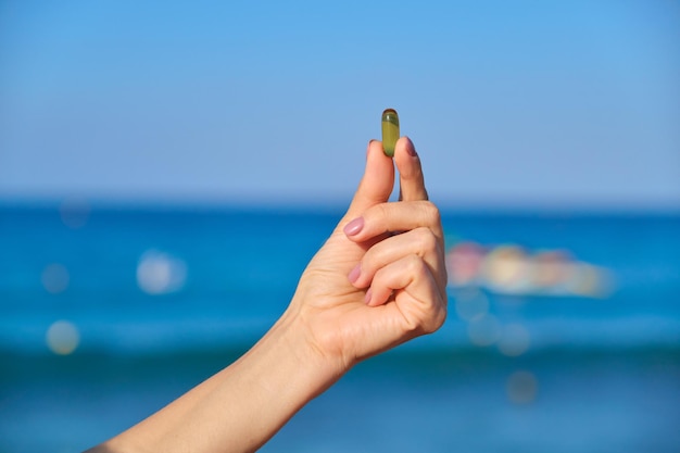 Capsula di vitamina d, e, a, omega 3, olio di pesce nel primo piano della mano. mare blu, sfondo del cielo. alimentazione sana, medicina, stile di vita, concetto di integratori alimentari