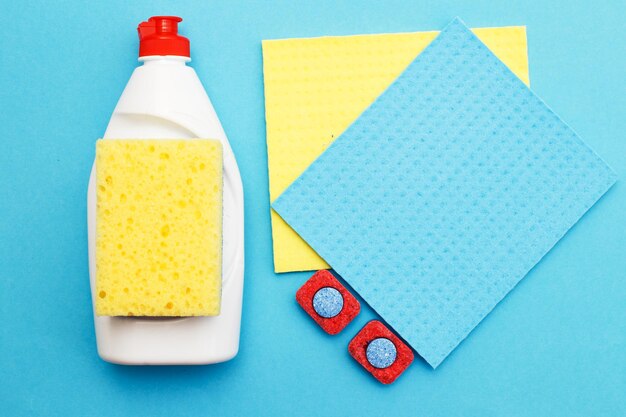 Capsules for dishwashers, dishwashing detergents liquid, kitchen rag and sponges on a blue background. flat lay