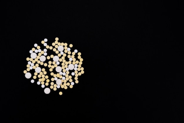 Capsules and tablets of white and yellow color. Black background. Health concept