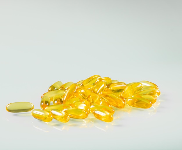 Capsules of yellow fish oil gel reflected on glass background