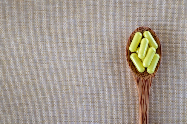 Capsules yellow Quercetin in a wooden spoon on a beige background Top view copy space