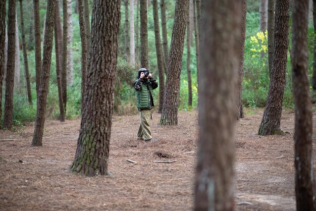 Плененный мальчик с камерой в лесу. Школьник в пальто и панаме фотографирует, гуляет. Детство, природа, концепция досуга