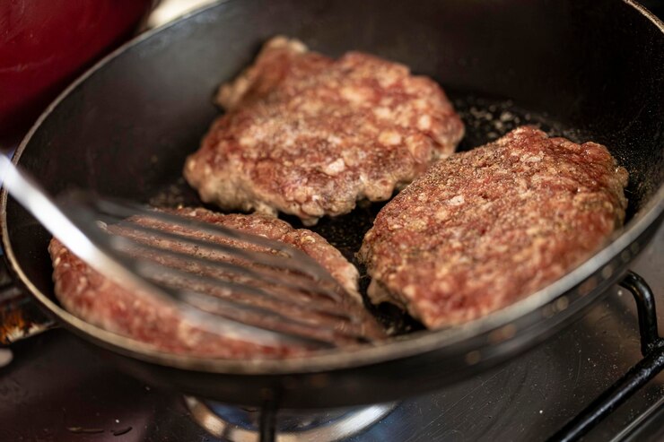 Photo 家庭用コンロの上のフライパンでジューシーなハンバーグパティがジュウジュウと焼ける瞬間を撮影