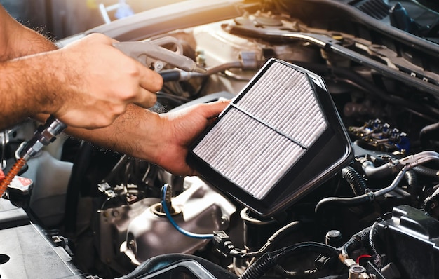 Photo car air filter in auto mechanic hand is blowing dust and cleaning with air blow gun