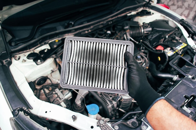 Photo the car air filter is clogged and there are stains on the air filter in the hands of the car mechanic with car engine compartment background automotive maintenance concept