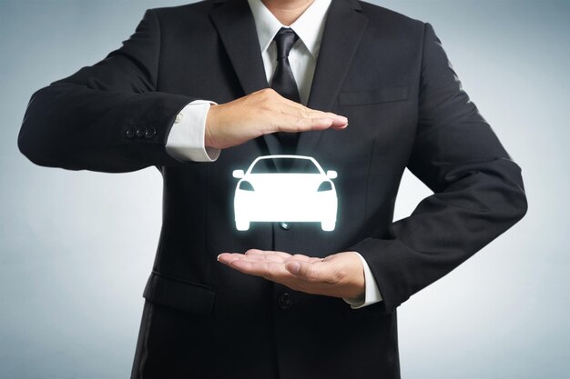 Car automobile insurance and collision damage waiver concepts Businessman with protective gesture and icon of car Wide banner composition and bokeh in background